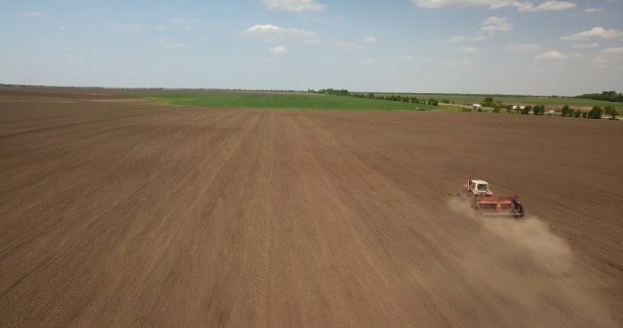 Farmer in tractor preparing land with seedbed cultivator against the blue sky